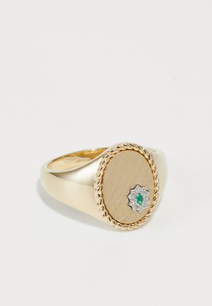 Gold ring featuring a round, brushed metal face, a central diamond star accent, and an emerald, surrounded by a twisted band detail.