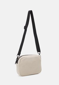 Borsa crossbody in corda beige con forma rettangolare, tracolla nera regolabile, chiusura con zip superiore e texture a coste.
