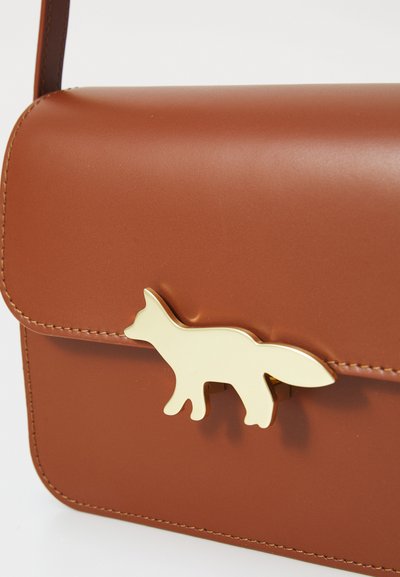 Borsa a tracolla in pelle sintetica marrone con un fermaglio a forma di volpe dorata, superficie liscia, forma rettangolare e dettagli cuciti lungo i bordi.