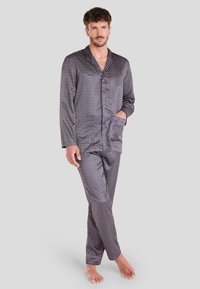 Conjunto de pijama para hombre en un tejido liso y oscuro con un patrón geométrico en rojo y blanco. La parte superior cuenta con un cuello de solapa y botones; los pantalones tienen una cintura elástica.