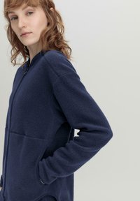Marineblaue Fleecejacke mit durchgehendem Reißverschluss, langen Ärmeln und seitlichen Taschen. Sie hat eine strukturierte Oberfläche und eine lockere Passform.