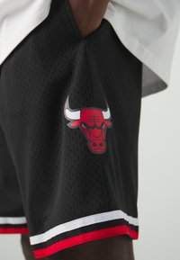 Shorts sportivi neri realizzati in tessuto a rete, con tasche laterali e un logo rosso e bianco dei Bulls sulla gamba sinistra, completi di strisce a contrasto sull'orlo.
