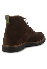 Botas de tobillo de ante marrón con punta redonda, costuras en contraste y una cinta verde en el talón. Suela de goma negra para un buen agarre.