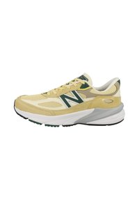 Zapatillas de ante y malla en color amarillo y crema con detalles verdes, suela intermedia blanca y suela exterior negra. Presenta una punta redondeada y un cuello acolchado.