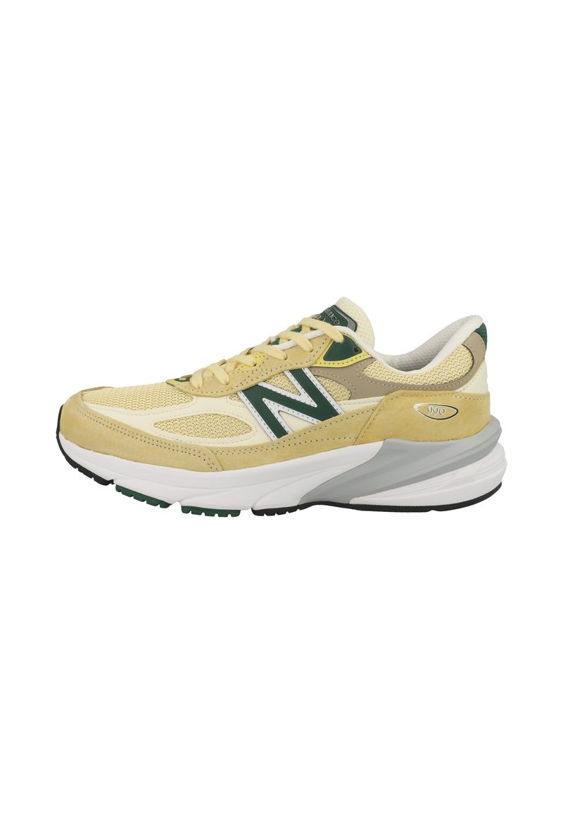 Zapatillas de ante y malla en color amarillo y crema con detalles verdes, suela intermedia blanca y suela exterior negra. Presenta una punta redondeada y un cuello acolchado.