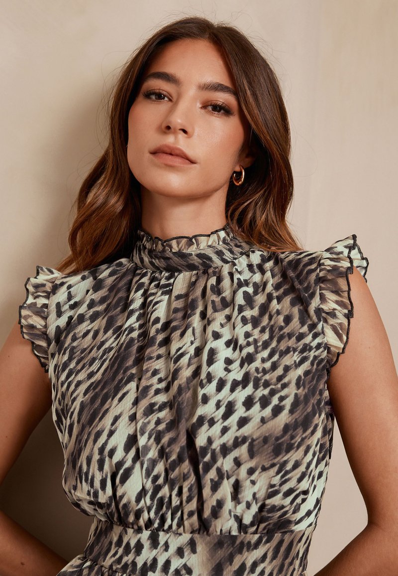 Sleeveless dress featuring a frilled collar, patterned in shades of cream and black, with a slightly sheer texture and gathered waist detail.