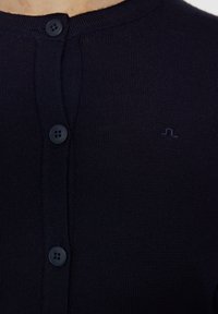 Merinovillan villatakki, jossa on teksturoitu neule, pyöreä pääntie ja neljä nappia, sekä pieni logo brodeerattuna rintaan.