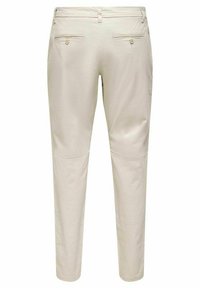 Pantalons beiges avec une texture lisse, présentant deux poches arrière avec boutons et un design ajusté. La ceinture inclut des passants de ceinture.