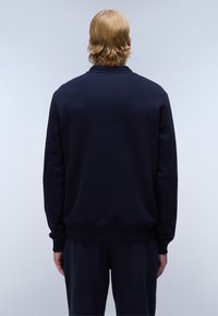 Marineblauwe sweatshirt met een geribbelde kraag en manchetten, gemaakt van een gladde stof. Heeft een relaxte pasvorm en is gezien vanuit de achterkant.