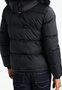 Black puffer jacket with a quilted design, featuring a fur-lined hood, elastic cuffs, and a smooth, shiny texture.
