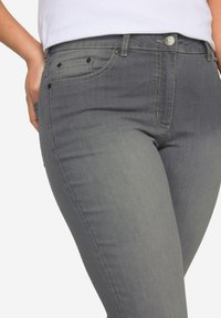 Jean en denim gris au design ajusté, avec poches avant, coutures contrastées et fermeture à bouton. Texture lisse et forme cintrée.