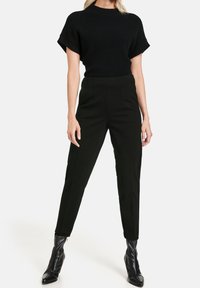 Haut en maille côtelée noire à manches courtes, associé à un pantalon noir taille haute et sur mesure, et des bottines noires à bout pointu.