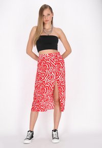 Piros szoknya fehér absztrakt mintával, oldalsó hasítékkal, fekete crop top-pal és fekete sportcipővel párosítva. Simító anyag, középhosszú kialakítás.