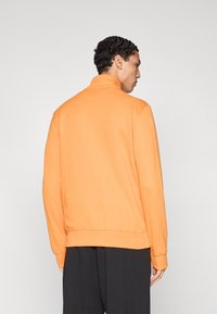 Πορτοκαλί φούτερ με ψηλό γιακά, απαλή υφή, ριμπ μανσέτες και τελείωμα. Ο σχεδιασμός διαθέτει άνετη εφαρμογή και μινιμαλιστικό στυλ.