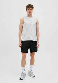 Lys grå ærmeløs træningstop med et subtilt mønster, parret med sorte shorts og sølv sneakers. Hvide sokker med logodetaljer synlige.