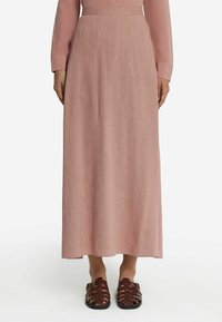 Ljusrosa maxiklänning med en mjuk textur, långa ärmar och en åtsittande midja. Kombinerad med bruna sandaletter med remmar.