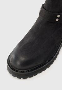 Stivale alla caviglia nero con tomaia in suede liscia, punta tonda, finitura opaca e suola robusta con un leggero tacco e cuciture a vista.