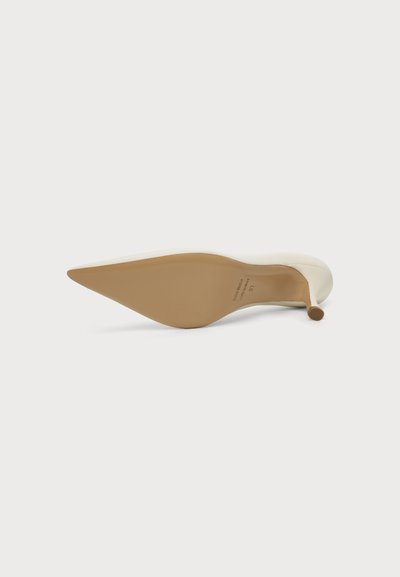 Chaussure à talon haut beige couchée sur le côté, montrant la semelle pointue et le talon fin sur fond blanc.