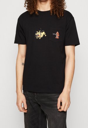 Person iført sort T-shirt med tegneseriehundegrafik nær brystet og orange brandhane-grafik på lommen.