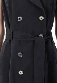 Σκούρο μπλε παλτό με διπλό κούμπωμα, μεγάλους ασημένιους κουμπιά, ζώνη από ύφασμα και ελκυστική υφή.