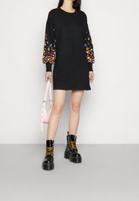 Vestido sudadera negro con mangas largas de patrón floral. Combinado con botas negras de cordones y un bolso rosa. Textura suave, diseño casual.