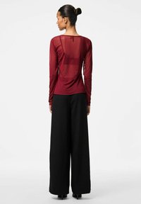 Långärmad, burgundy genomskinlig topp med rund halsringning, kombinerad med vida svarta byxor. Tyget har en slät yta och en subtil lyster.