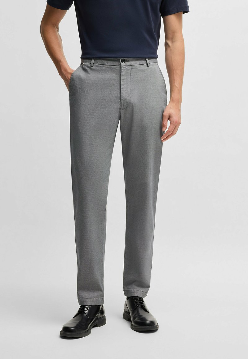 Gray patterned trousers made from textured fabric. Features a button closure and side pockets, paired with polished black shoes.