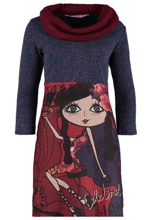 Woman walking in a dark blue dress with a colorful cartoon girl print, black tights, black ankle boots, and carrying a large tan suede shoulder bag.
