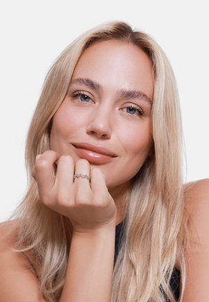 Anello zigzag in argento con accenti in pietre preziose colorate, indossato su una mano con una manicure naturale, su uno sfondo bianco semplice.
