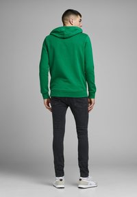 Felpa con cappuccio verde dal finish texturizzato, dotata di una tasca a marsupio e polsini a costine, abbinata a jeans scuri e sneakers bianche.
