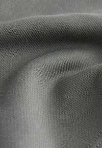 Texturerat, stretchigt tyg i en dämpad grå färg. Visar ett fint stickat mönster med subtil lyster och jämn yta, något skrynklig.