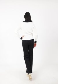 Pull en maille blanche avec des détails noirs au col et aux poignets, associé à un pantalon noir taille haute et des talons beiges. Modèle de dos.