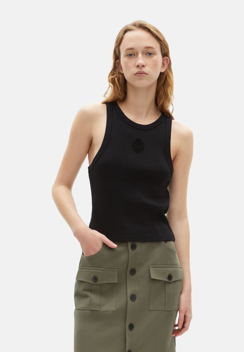 Zwarte geribde tanktop met een ronde hals en een logo aan de voorkant, gecombineerd met een olijfgroene rok met grote opgestikte zakken en knopen.