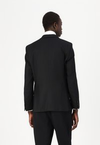 Veste de costume noire, design sur mesure, tissu lisse, fente unique à l'arrière, avec des poignets à boutons et des revers aiguisés.