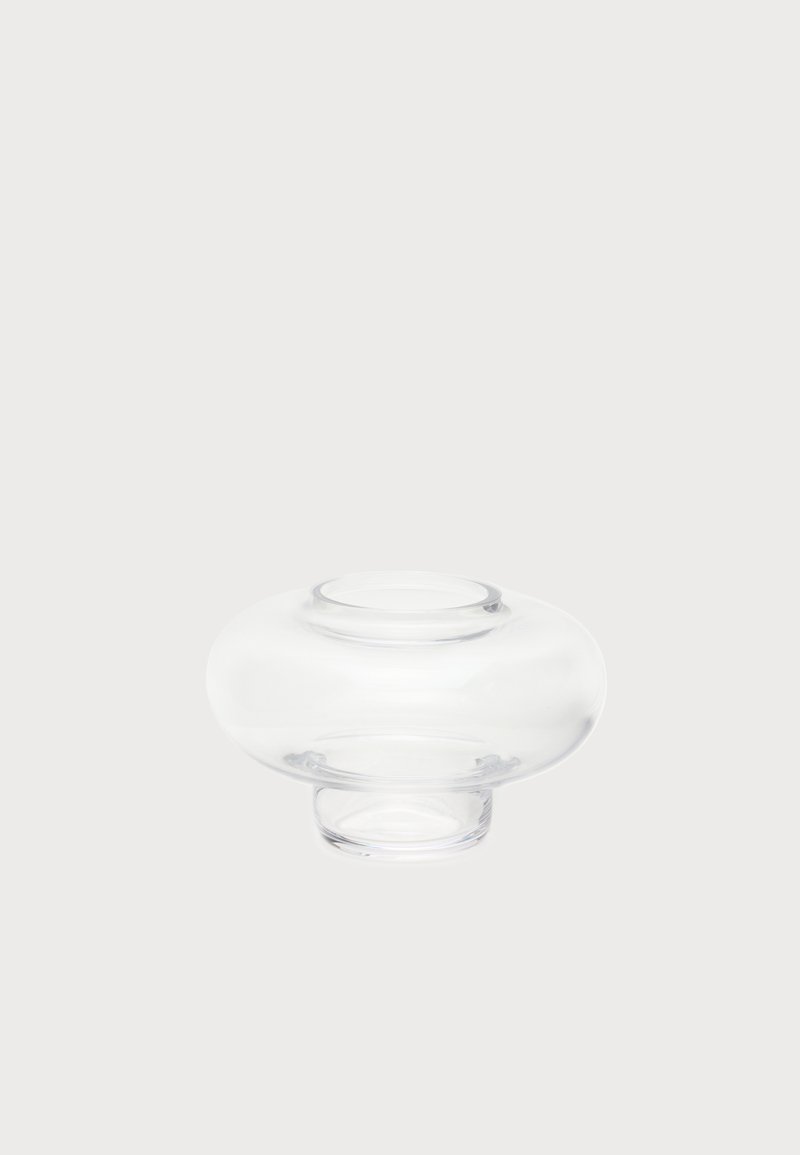 Vase en verre clair avec un milieu large et arrondi et des ouvertures étroites en haut et en bas, posé sur un fond clair uni.
