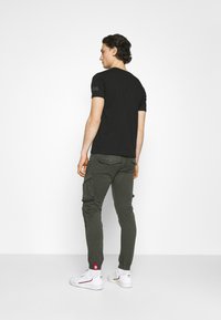 Zwarte T-shirt met korte mouwen en een ronde hals, gecombineerd met groene cargo broek met meerdere zakken en ribgebreide boorden, en witte sneakers.