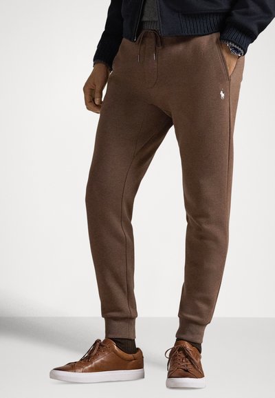 Bruine joggingbroek met een taillekoord en zijzakken, voorzien van een logo-accent. Gecombineerd met bruine sneakers en gestructureerde bruine sokken.