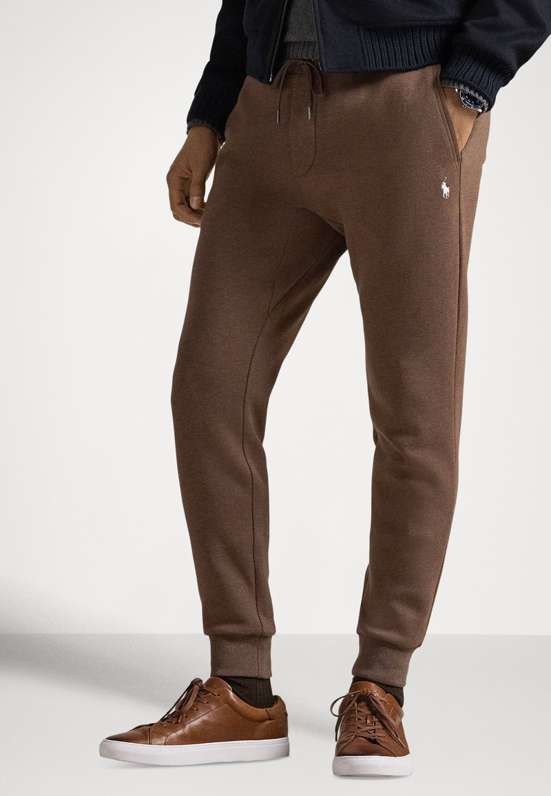 Brązowe spodnie dresowe ze sznurkiem w pasie i bocznymi kieszeniami, z akcentem z logo. Połączone z brązowymi trampkami i teksturowanymi brązowymi skarpetkami.