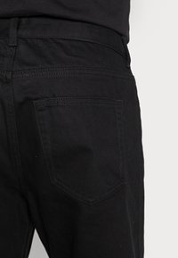 Black denim jeans with a smooth texture, featuring a standard back pocket and subtle stitching details, shown from the back view.