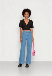 Top cropped preto com mangas curtas, jeans de perna larga azuis e sandálias plataforma pretas. Segurando uma pequena bolsa rosa.