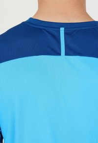 Kortärmad atletisk skjorta med en blå överdel och en ljusare blå nederdel med en subtil textur och en prydlig söm på baksidan.