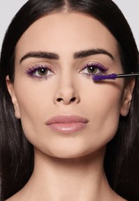 Fioletowy tusz do rzęs nałożony na rzęsy, podkreślając elegancki czarny aplikator. Gładka skóra i naturalny kolor ust dopełniają wygląd.