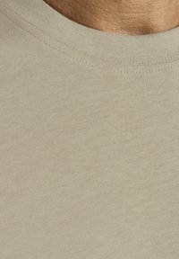 Beige cotton crewneck T-shirt featuring a ribbed neckline and soft, smooth texture with slightly visible stitching.