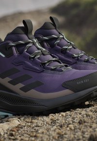 Purple waterproof hiking shoes with black accents, textured surface, and laces. Features a thick sole and prominent brand markings.