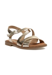 Sandalias metálicas doradas con tiras entrecruzadas, suela plana y cierre de hebilla. Plantilla de textura suave y suela marrón con detalle de costura.