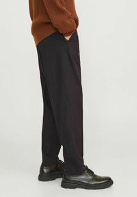 Pantalones morados oscuros, de corte holgado, con bolsillos laterales, combinados con zapatos negros con cordones. La tela parece suave con un ligero brillo.
