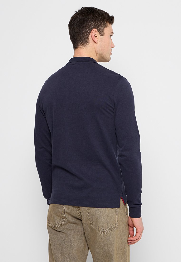 Polo a maniche lunghe blu navy in cotone con colletto classico, aperture laterali e un piccolo dettaglio rosso all'orlo. Vista posteriore mostrata.