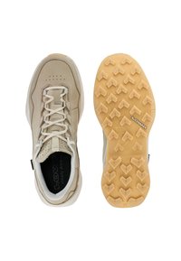 Béžová turistická bota s bílými tkaničkami a polstrovaným límcem vedle podrážky, která má hnědý gumový běhoun s úhlovými vzory a logem "Lowa".