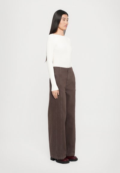 White ribbed long-sleeve top paired with brown wide-leg trousers. Trousers feature a front button, zipper, and side seams. Dark shoes complete the look.