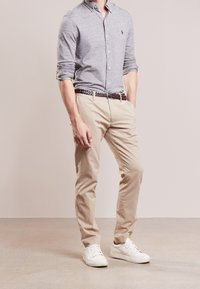 Szara koszula z długim rękawem i kołnierzykiem zapinanym na guziki, w połączeniu z jasnobeżowymi chinosami i białymi sneakersami. Posiada pleciony brązowy pasek.